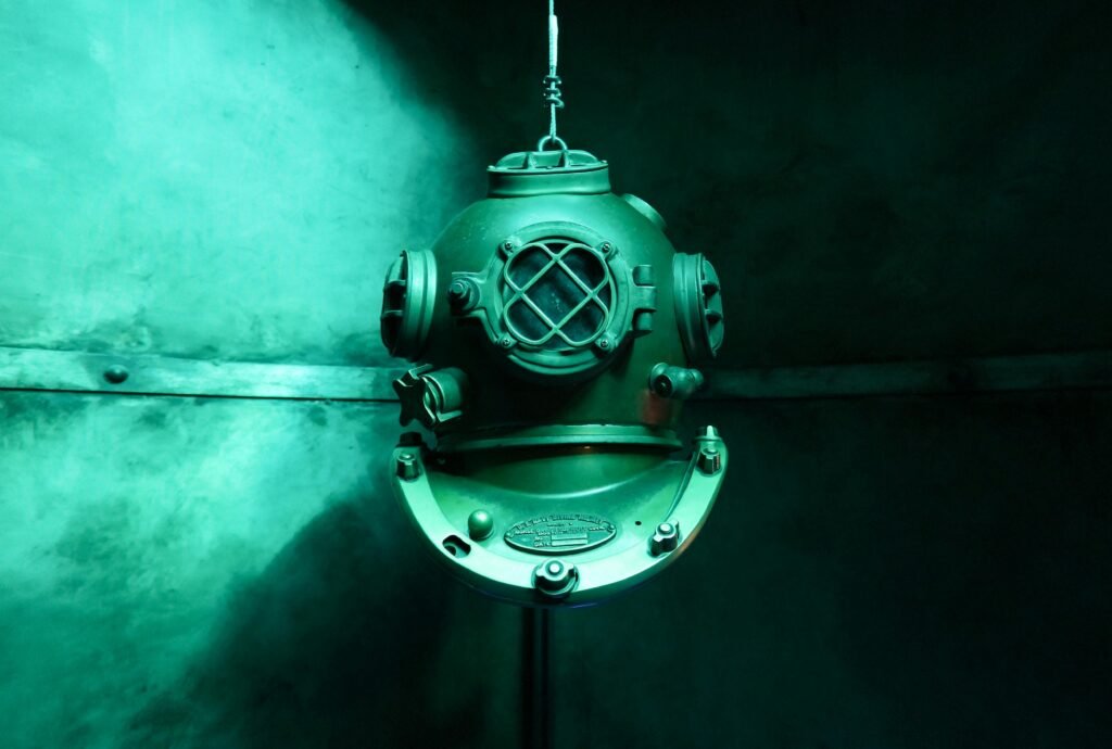 Close-up of a vintage diving helmet illuminated by aqua green lighting, showcasing maritime history.